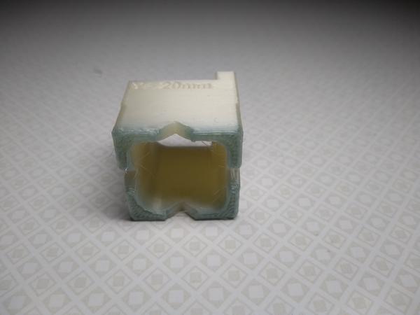 A 3D printed calibration cube, mainly white, but showing a dark discoloration on the bottom.
