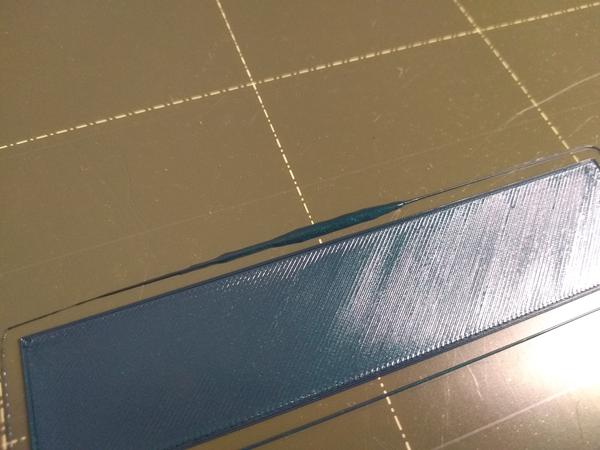 A rectangular one-layer calibration print on a smooth print sheet. The skirt shows a thick blob where much more material has been extruded than expected.