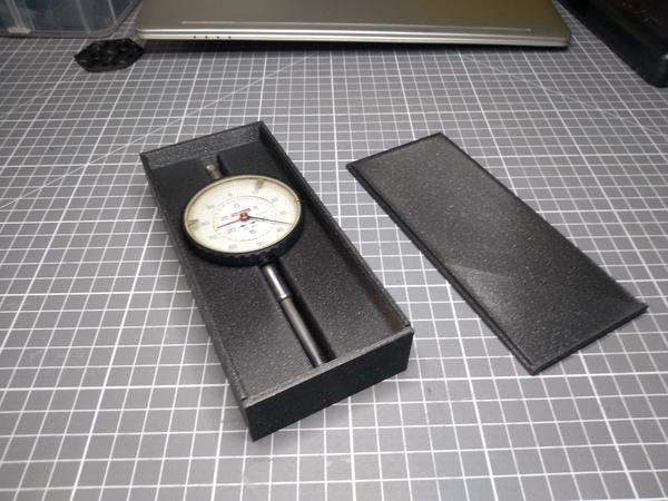 An open box with a dial indicator inside it.