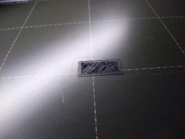 A rectangular one-layer calibration print, photographed at a low angle. There are ridges visible where the nozzle dragged through the material.
