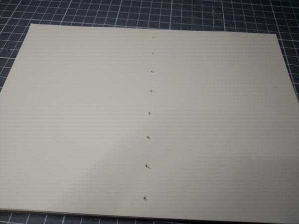 A close-up of a stack of paper, holes drilled into it.